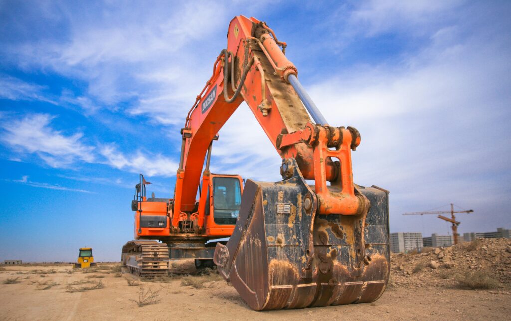 A large orange excavator working on a construction site under a blue sky.